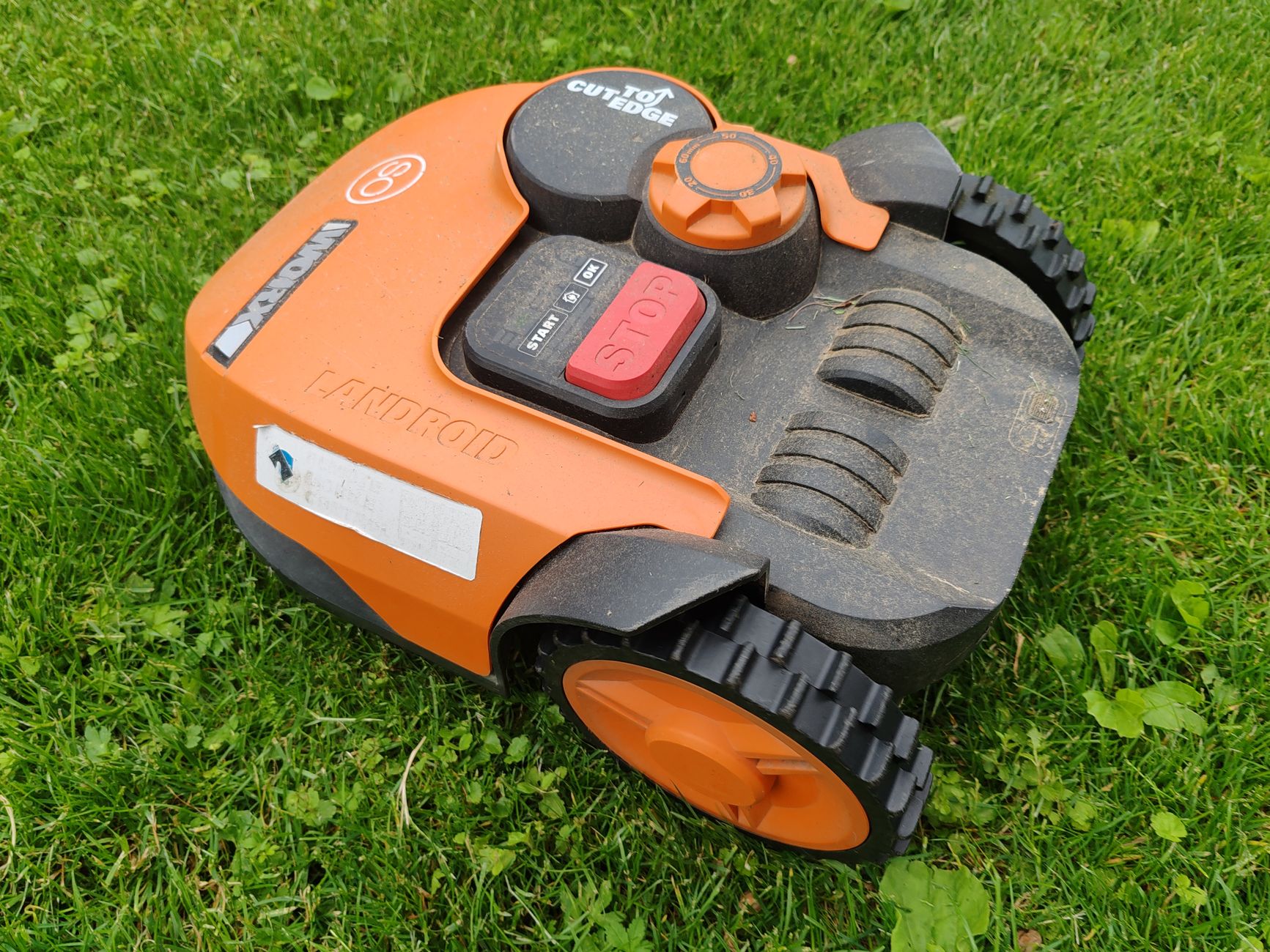 A modern robotic lawn mower in vibrant orange resting on a green lawn, ready for automated mowing tasks.