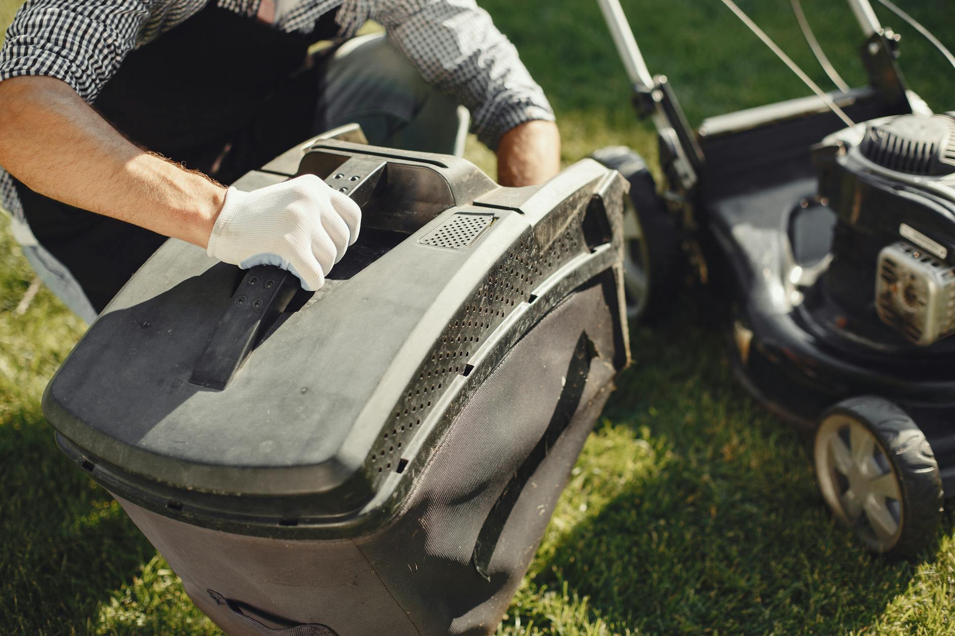 An adult man replacing a lawn mower bag on a sunny day in the yard.